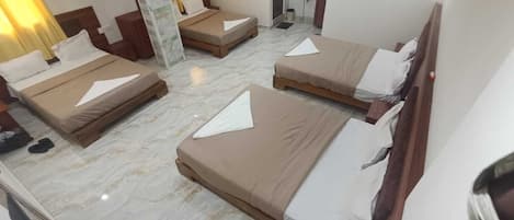 A hotel room with four beds arranged in a square layout, a marble floor, and a wooden headboard.