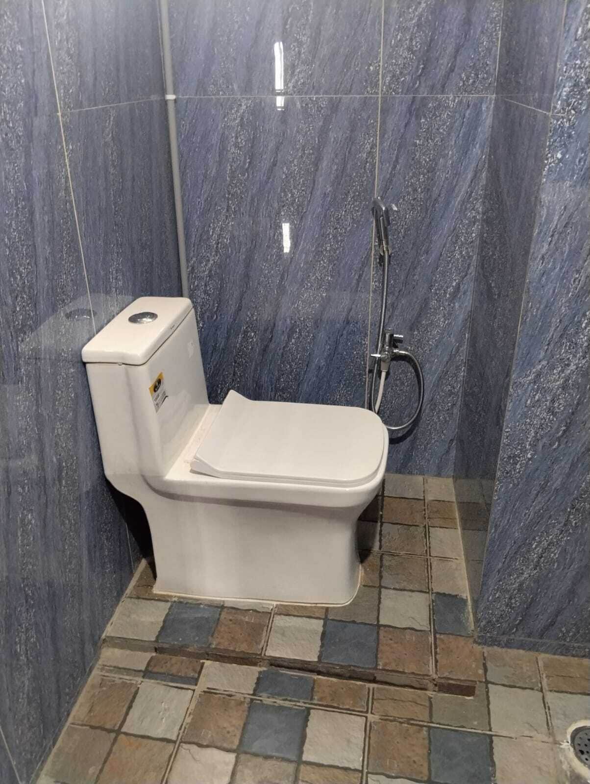 A bathroom with a white toilet, a shower area, and tiled walls.