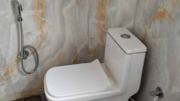 Un baño con inodoro, ducha y pared de mármol.