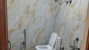 A bathroom with a toilet, a shower, and a marble wall. - Hotel Udupi Palace (Mysore)