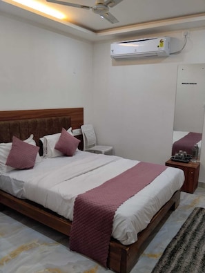 Quarto de hotel com uma cama, mesa de cabeceira, cadeira, ar condicionado e ventoinha de teto.
