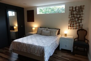 Ein Schlafzimmer mit einem Bett, zwei Nachttischen, einem Sessel, einem Fenster und einem Wandbild.
