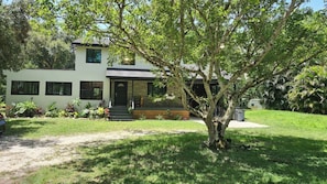 A two-story house with a front porch, surrounded by a well-maintained lawn and various plants. - Earthy with a Pop of Bling House Nestled in beautiful Jupiter Farms, FL. (Jupiter)