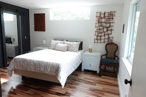 A bedroom with a bed, bedside tables, a chair, a wall art piece, and a window.