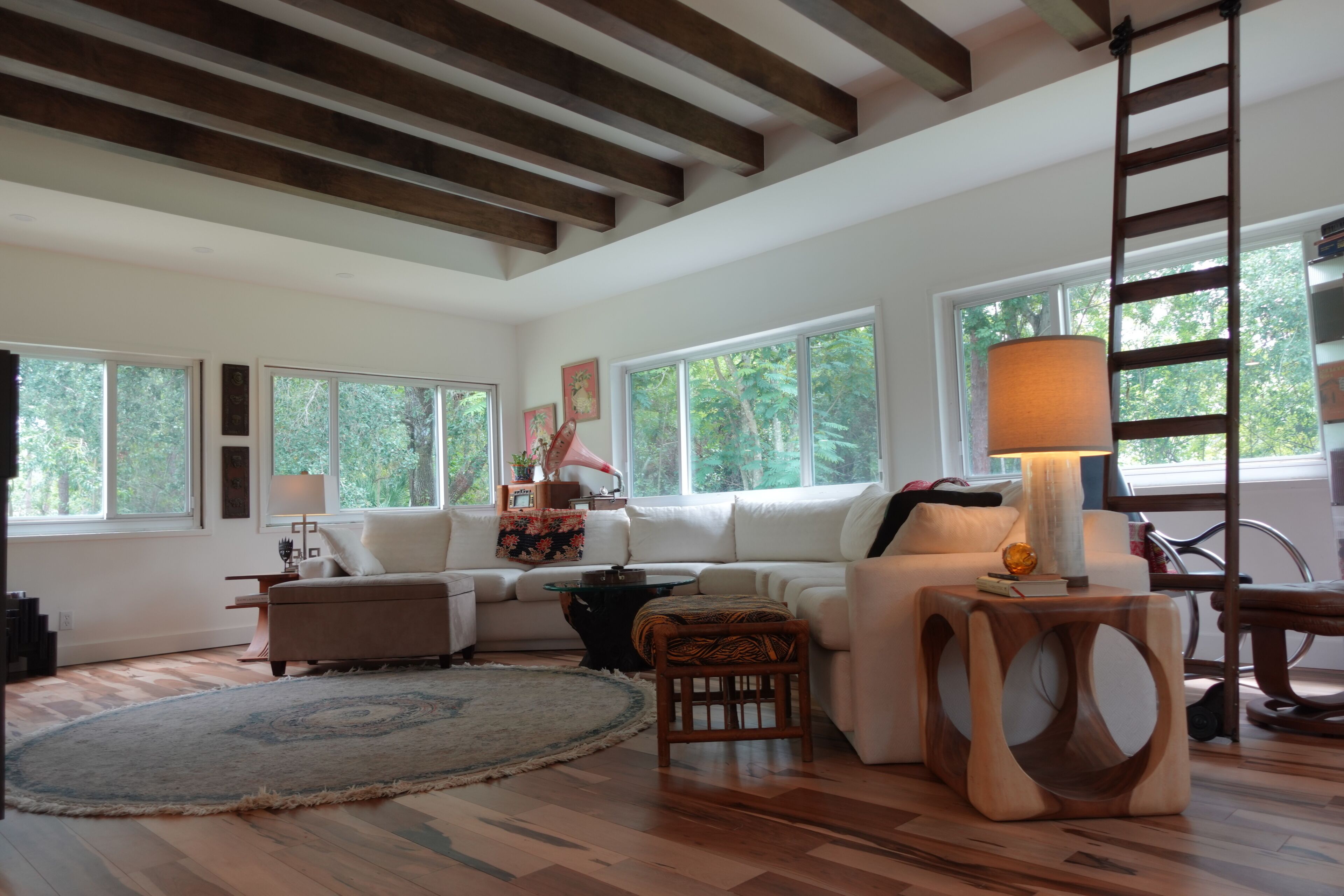 Un salón amplio con techo alto, ventanas grandes, un conjunto de sofás, una mesa de centro y piso de madera.