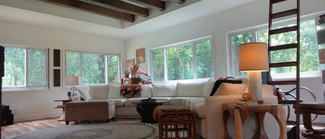 Un salón amplio con techo alto, ventanas grandes, un conjunto de sofás, una mesa de centro y piso de madera.