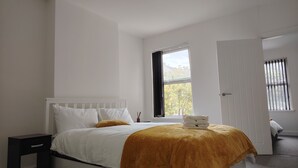 A bedroom with a bed, a nightstand, a window with curtains, and a door. - Modern 3‑Bed Home Near Dudley Zoo, Black Country Museum & Russell Hall Hospital (Dudley)