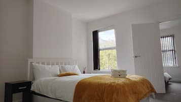 A bedroom with a bed, a nightstand, a window with curtains, and a door.