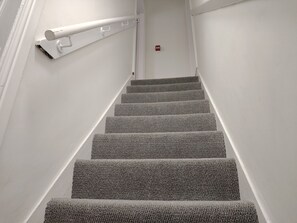 Eine Treppe mit Teppichstufen und einer Handlauf, die zu einer Tür mit Rauchmelder führt.