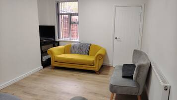 A living room with a yellow sofa, a grey sofa, a TV, and a window with bars.