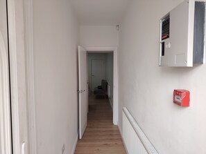 A hallway with a radiator, a door, and a red fire alarm box. - Modern 3‑Bed Home Near Dudley Zoo, Black Country Museum & Russell Hall Hospital (Dudley)