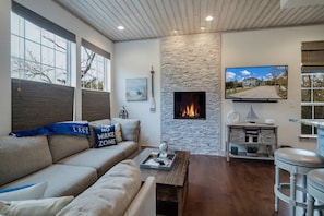 A living room with a stone fireplace, a sofa with decorative pillows, a coffee table, and a television mounted on the wall.