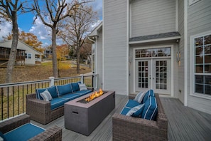 A covered outdoor deck with a fire pit, wicker furniture, and a view of a residential area.