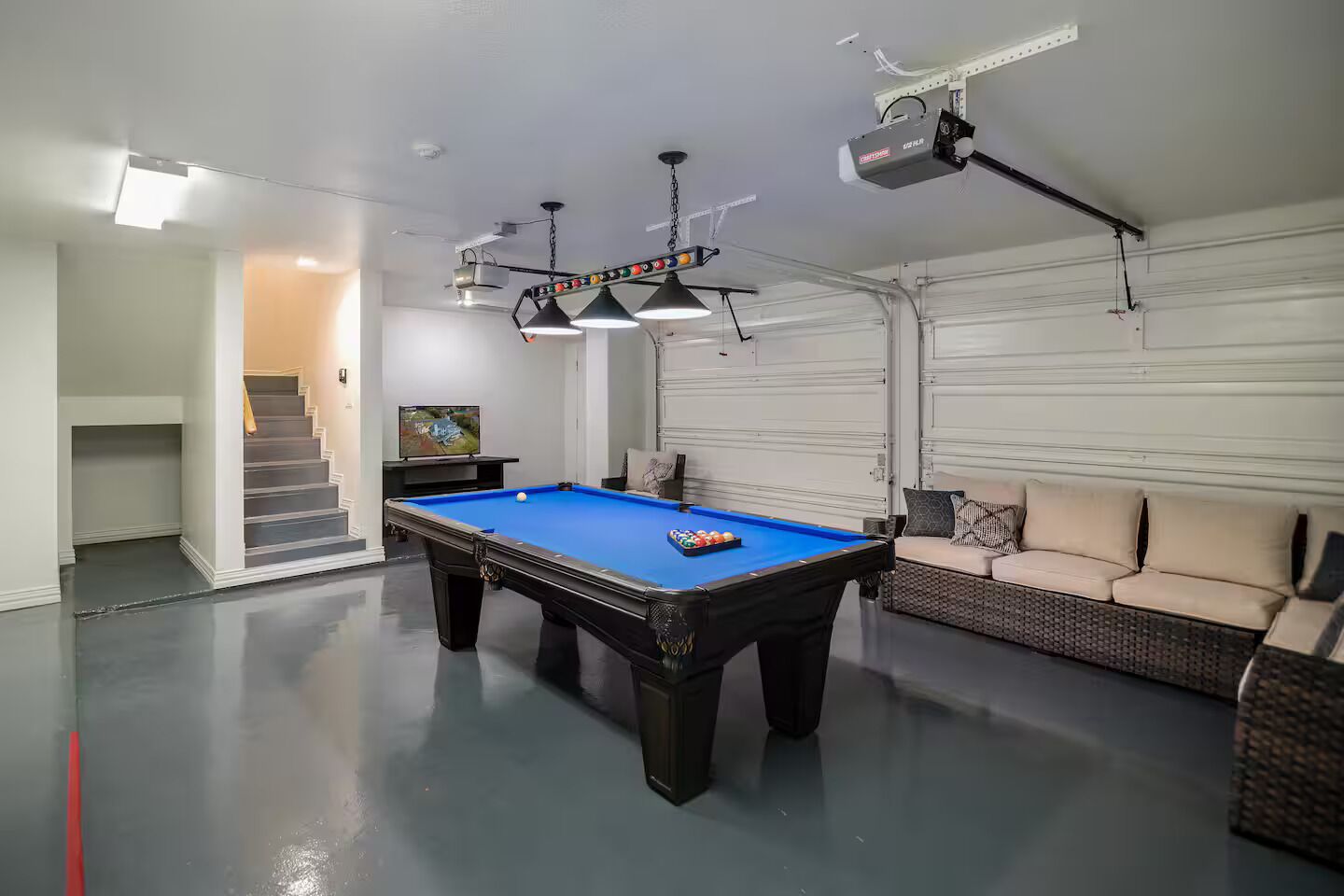 Une table de billard dans une pièce où se trouvent un canapé et un téléviseur.