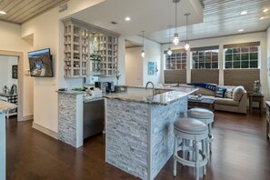 A modern kitchen with a central island, bar stools, and a dining area with a sofa and coffee table.