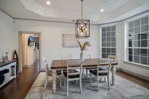 A dining area with a wooden table, white chairs, a vase with dried plants, and a modern pendant light. - Luxury 4BR/5BA Lakefront Oasis with Expansive Decks and Panoramic Views (Pottsboro)