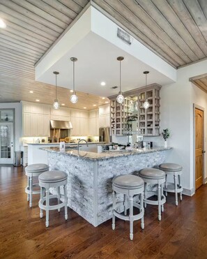 A modern kitchen with a large island, bar stools, and pendant lighting.
