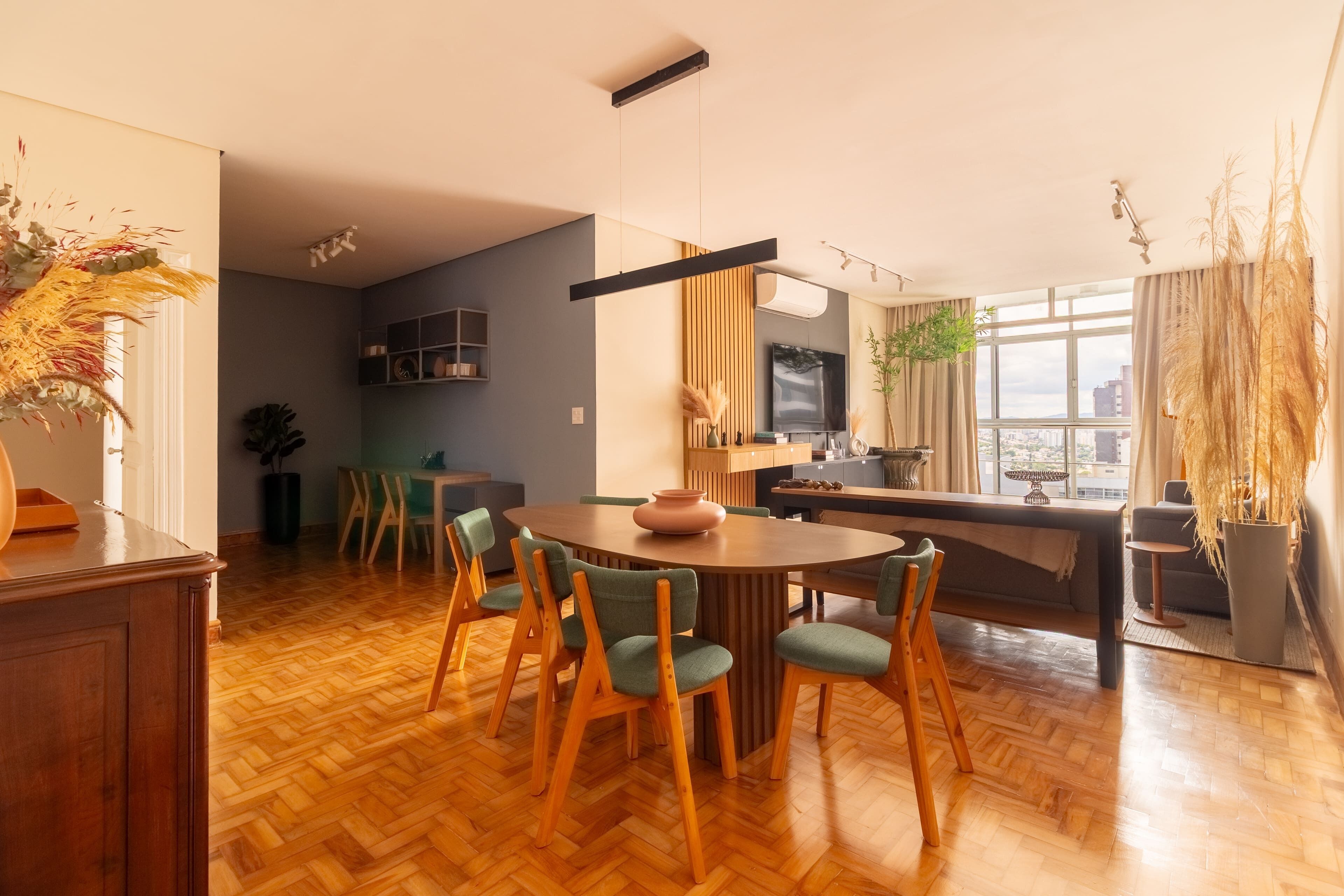 A modern kitchen with a dining area, wooden flooring, and a large window with a city view.