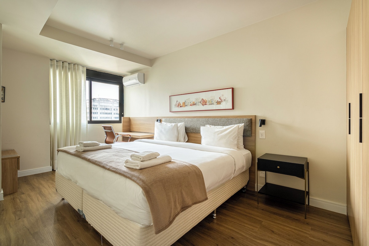 Ein Hotelzimmer mit einem großen Bett, einem Nachttisch, einem Stuhl und einem Fenster mit Vorhängen.