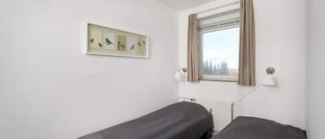 Una habitación con dos camas individuales, una ventana con cortinas, una lámpara de pared y un cuadro con pájaros.