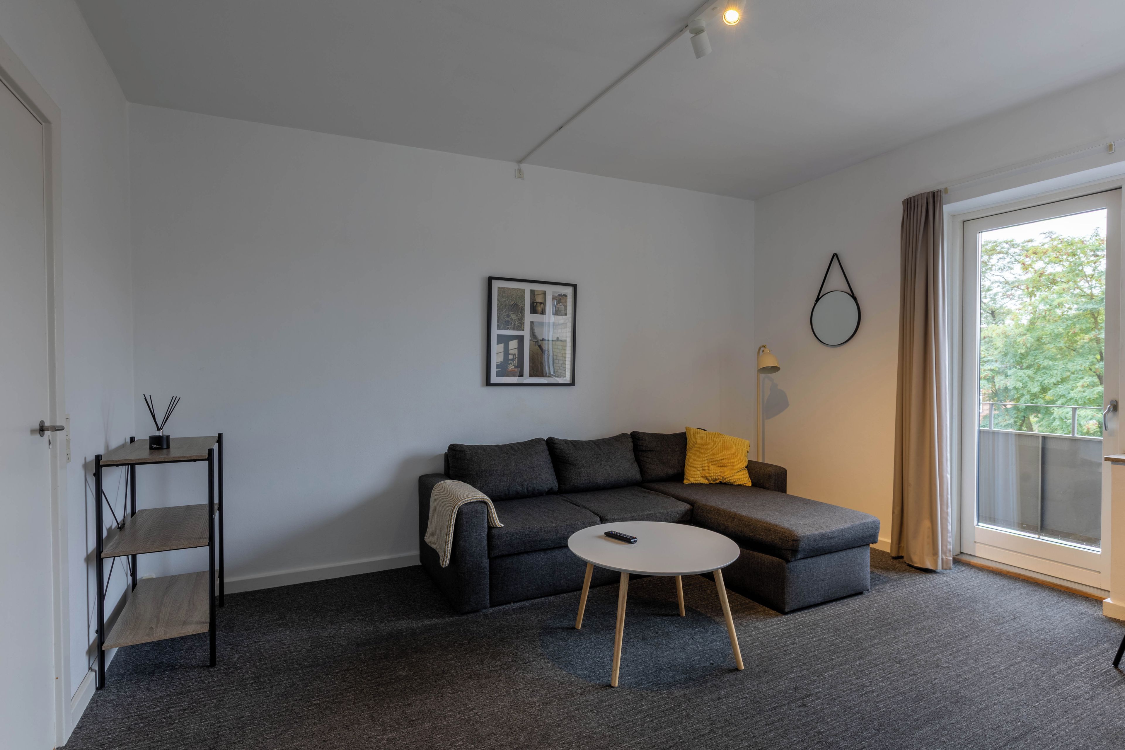 A modern living room with a grey sofa, a small round table, and a picture frame on the wall.