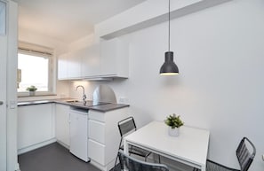 A compact kitchen with white cabinets, a built-in dishwasher, a white dining table with two chairs, and a pendant light.