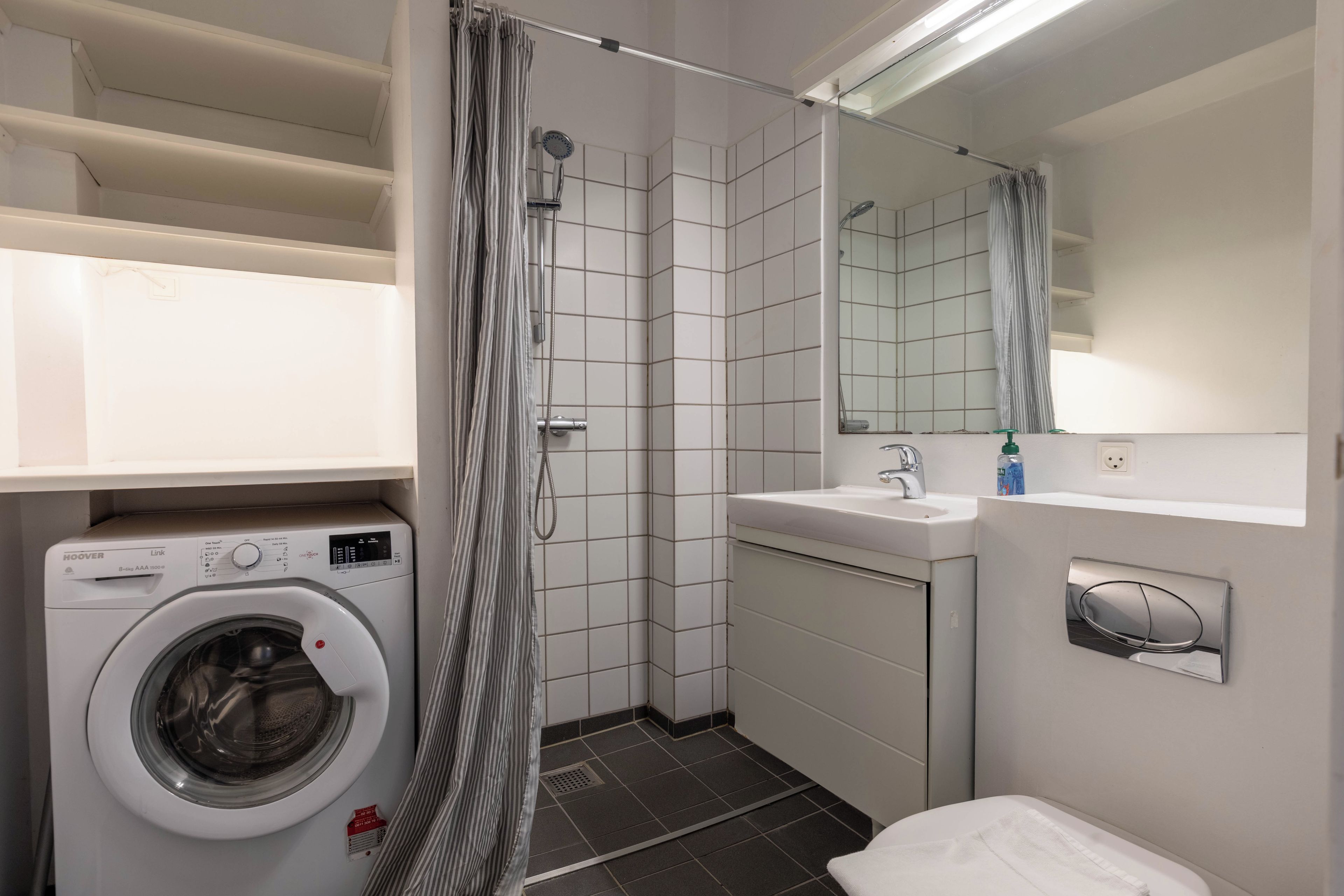 A compact bathroom with a washing machine, a shower, and a sink.