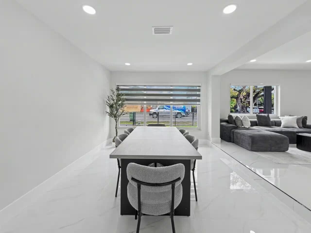 A modern conference room with a long table and chairs, a sofa set, and a large window with a view of the street.