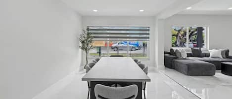 A modern conference room with a long table and chairs, a sofa set, and a large window with a view of the street.