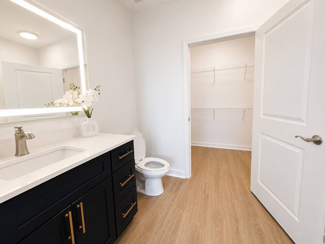 Une salle de bain avec un lavabo blanc, des meubles noirs, des toilettes blanches et un miroir avec un éclairage intégré.
