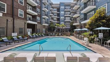 A swimming pool with lounge chairs and umbrellas, surrounded by multi-story buildings with balconies.