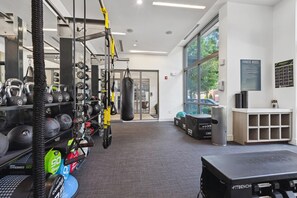 A gym with weightlifting equipment, a punching bag, and a bench. - Luxury 2BR Near Uptown | Pool, Gym, BBQ (Charlotte)
