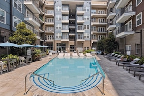 A modern apartment building with a central courtyard pool surrounded by lounge chairs and umbrellas. - Luxury 2BR Near Uptown | Pool, Gym, BBQ (Charlotte)