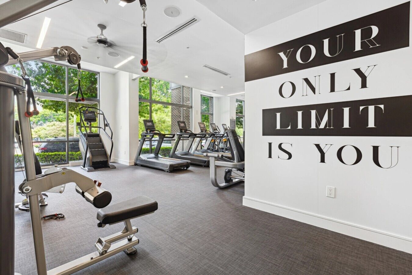 A gym with treadmills, a weight bench, and a motivational quote on the wall.