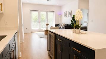 A modern kitchen with dark cabinetry, a light countertop, and a view to the living area.