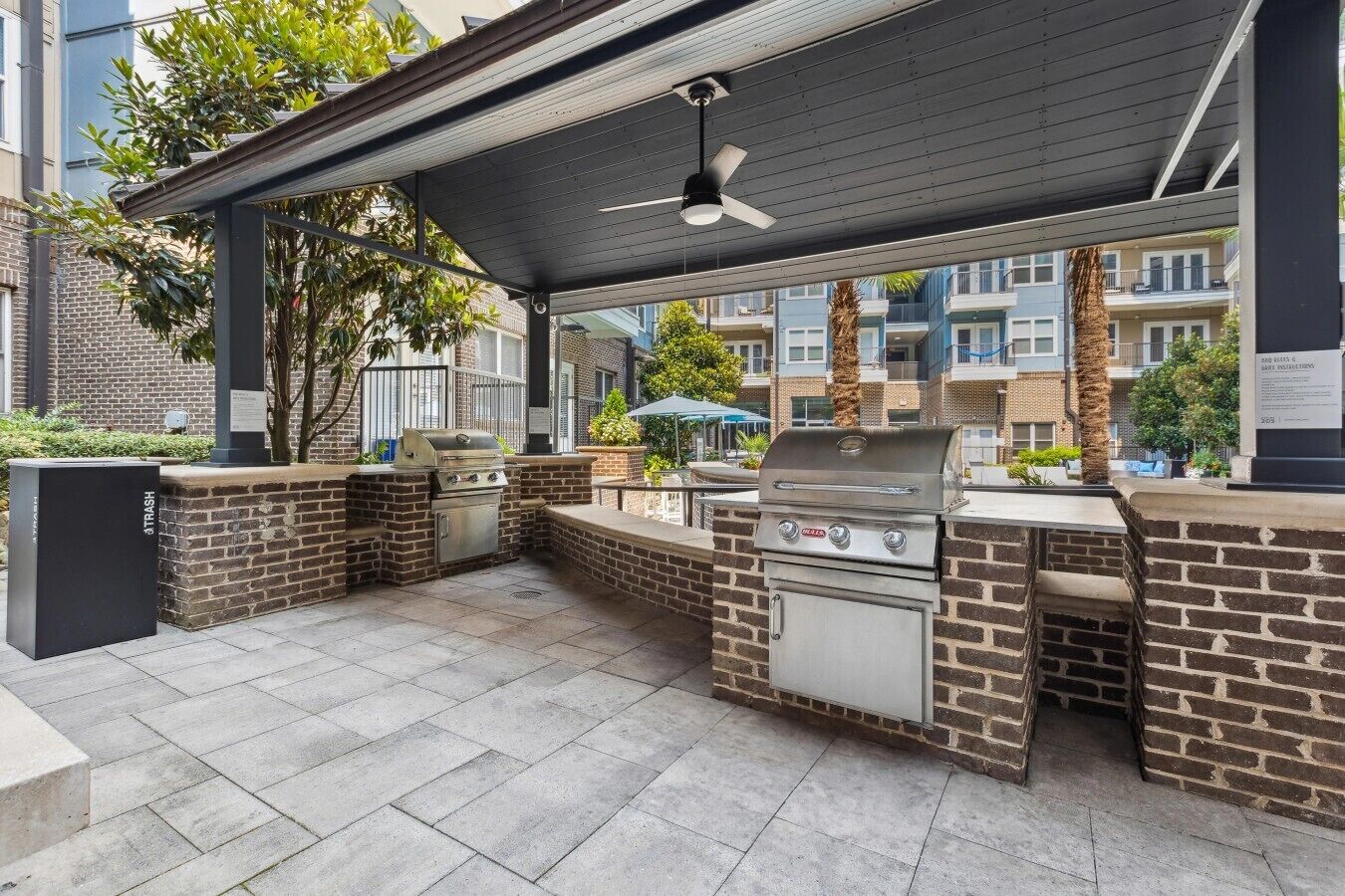An outdoor patio with a grill and seating area, surrounded by brick walls and a covered roof.