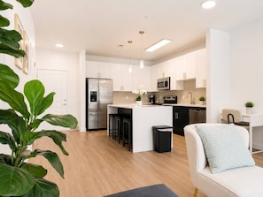 A modern kitchen with white cabinets, a stainless steel refrigerator, and a central island with bar stools. - Stylish 2BR Charlotte Stay | Pool, Gym & BBQ (Charlotte)