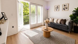 Ein modernes Wohnzimmer mit einer Couch, einem Couchtisch und einem großen Fenster mit Jalousien.