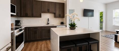 A modern kitchen with dark wood cabinets, stainless steel appliances, a central island with stools, and pendant lighting.