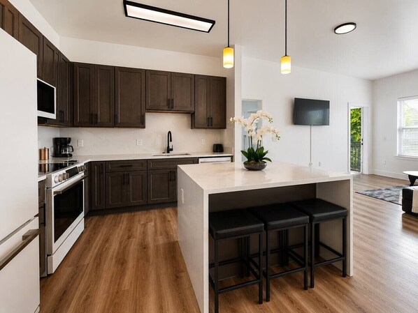 A modern kitchen with dark wood cabinets, stainless steel appliances, a central island with stools, and pendant lighting.