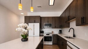 Een moderne keuken met donkere houten kastjes, een wit aanrecht, roestvrijstalen apparatuur en een centraal eiland met een orchidee in pot.