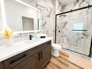 A modern bathroom with a marble backsplash, a glass shower enclosure, and a white toilet.