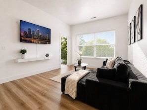 A modern living room with a black sofa, a coffee table, and a cityscape painting on the wall.