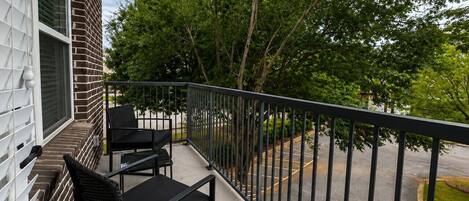 A balcony with two chairs and a table, overlooking a parking area and trees.