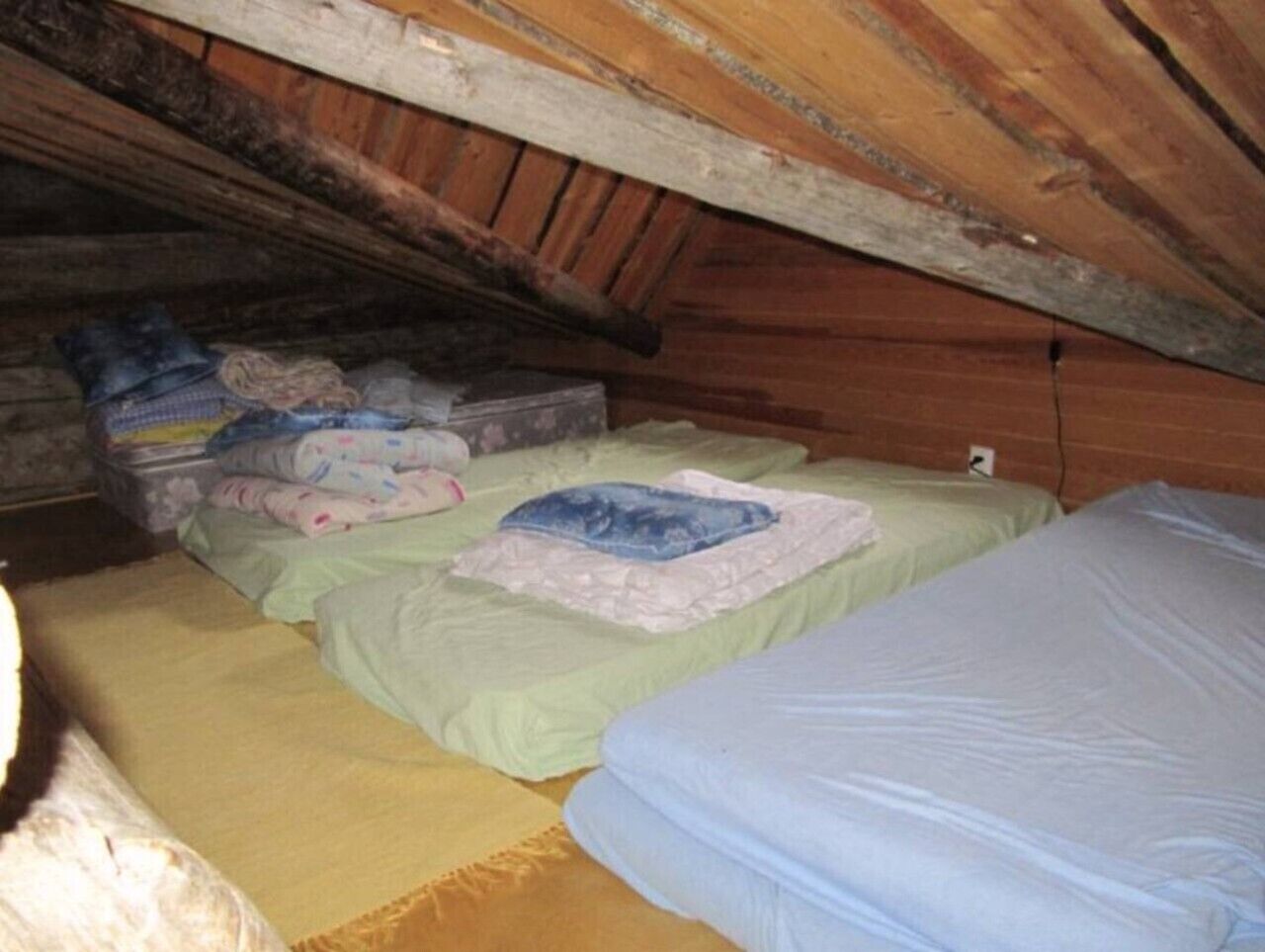 A small, dimly lit attic room with two beds, a wooden ceiling, and a wall-mounted heater.