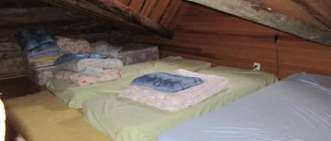 Een kleine, zwak verlichte zolderkamer met twee bedden, een houten plafond en een aan de muur bevestigde verwarming.