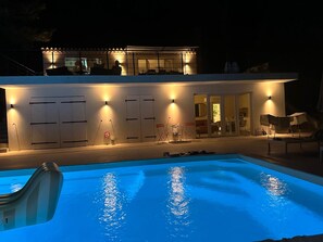 A swimming pool with a clear blue water surface, surrounded by a covered patio area with chairs and tables. - Villa Orange (La Croix-Valmer)