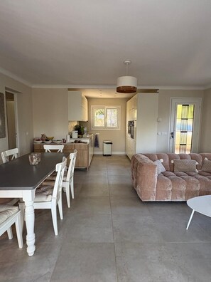 A spacious living area with a dining table, white chairs, a sofa, and a kitchen in the background. - Villa Orange (La Croix-Valmer)