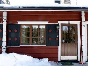 Eine Holzhütte mit brauner Tür und Fenstern, umgeben von Schnee.