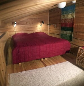 Ein Schlafzimmer einer Holzhütte mit einem Bett, einem weißen Teppich und einem farbenfrohen Wandteppich.